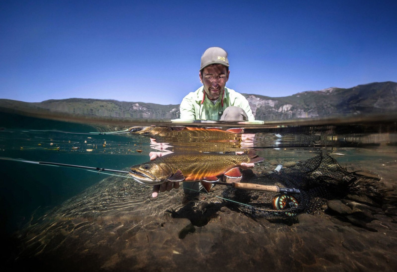 Underwater view of Emanuel Medina holding a trout in the clear water of a Patagonian lake while fly fishing in Bariloche, Argentina